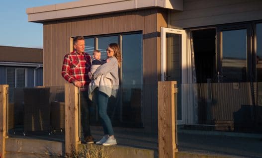 Couple with young child on balcony of the luxury lodge in the sun